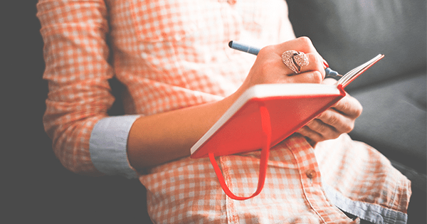 unrecognizable person writing in a red journal