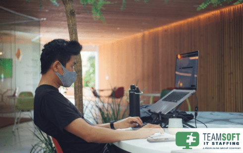 man wearing a mask sitting in front of laptop on raised stand