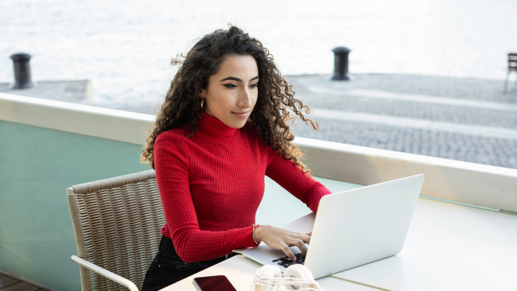 A woman sits at a table on a balcony working at a computer.